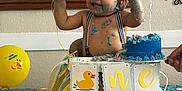 James joined the competition — help win amazing prizes! baby, balloon, banner, birthday, blue_frosting, cake, celebration, child, crown, decorations, face, feet, hand, highchair, indoor, messy, party, smiling, suspenders, tablecloth