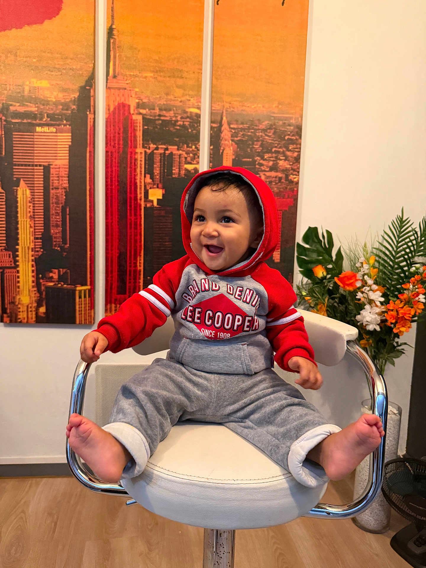 Kael a rejoint le concours — aidez-le/la à gagner de superbes lots ! toddler, child, smiling, hoodie, red_clothing, grey_pants, barefoot, chair, interior, wooden_floor, artwork, cityscape, flower_arrangement, plant, happy, indoor, person, furniture, portrait, casual_clothing