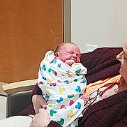 Corey is registered to the contest to win money with this photo: baby, newborn, blanket, colorful, sleeping, person, adult, holding, indoor, chair, clothing, pattern, peaceful, infant, portrait, human, wrapped, love, care, family