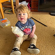 Lane joined the competition — help win amazing prizes! toddler, child, milk_bottle, carpet, indoor, sitting, blue_tshirt, pants, shoes, blonde_hair, furniture, drawer, television, chair, toy_box, face, person, home, floor, casual