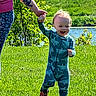 toddler, child, dinosaur_onesie, grass, adult_hand, tattoo, outdoor, sunny, greenery, pond, smiling, walking, nature, happy, person, daylight, holding_hand, baby, footwear, casual_wear