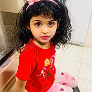 Mia is registered to the contest to win money with this photo: child, girl, headband, pink, red_shirt, heart_patterned_leggings, brown_eyes, curly_hair, indoors, kitchen, stool, tile_floor, countertop, cabinet, innocent_expression, sitting, person, portrait, cute, young