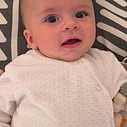 Naël a rejoint le concours — aidez-le/la à gagner de superbes lots ! baby, infant, white_clothing, face, eyes, plush_toy, blanket, pattern, lying_down, cute, smiling, skin, head, expression, child, indoors, soft_toy, fabric, closeup, person