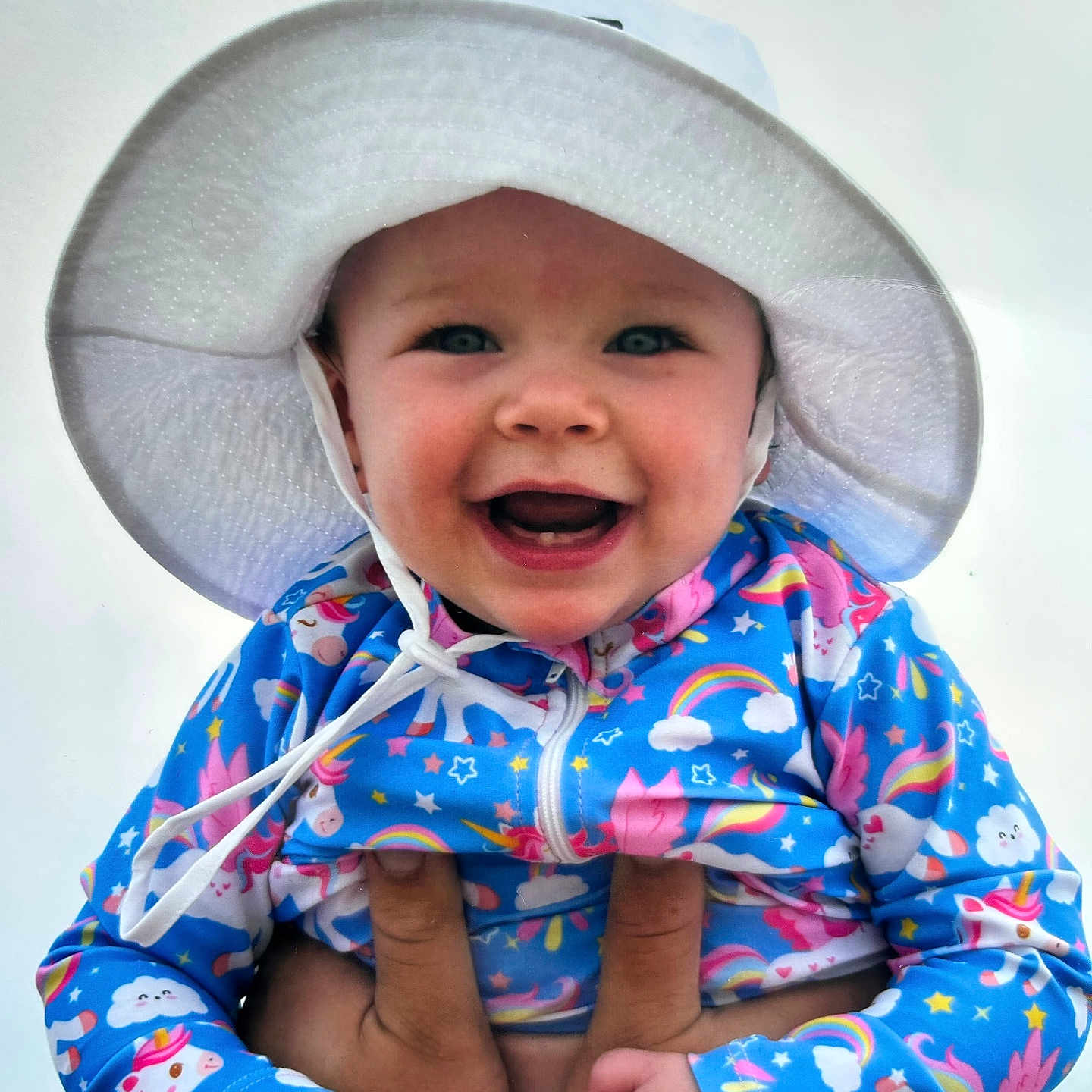 Harley is registered to the contest to win money with this photo: baby, blue_jacket, child, cloud, colorful_clothing, cute, hands, happy, hat, holding, infant, joyful, outdoor, person, portrait, rainbow, sky, smiling, unicorn, white_hat