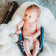 Brixton is registered to the contest to win money with this photo: baby, infant, baseball_glove, baseball, bat, blanket, carpet, diaper, blue, sports_equipment, soft_texture, cute, small, lying_down, indoors, person, newborn, relaxed, fingers, feet