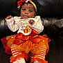 baby, infant, child, tutu, headband, bow, orange, white_clothing, striped_leggings, socks, black_leather_couch, cute, playful, festive, autumn, pumpkin_design, sitting, portrait, smiling, indoor