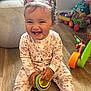 baby, bows, child, colorful, curly_hair, cute, floral_pajamas, furniture, happy, indoor, person, pigtails, playroom, playtime, sitting, smiling, stacking_rings, toddler, toys, wooden_floor