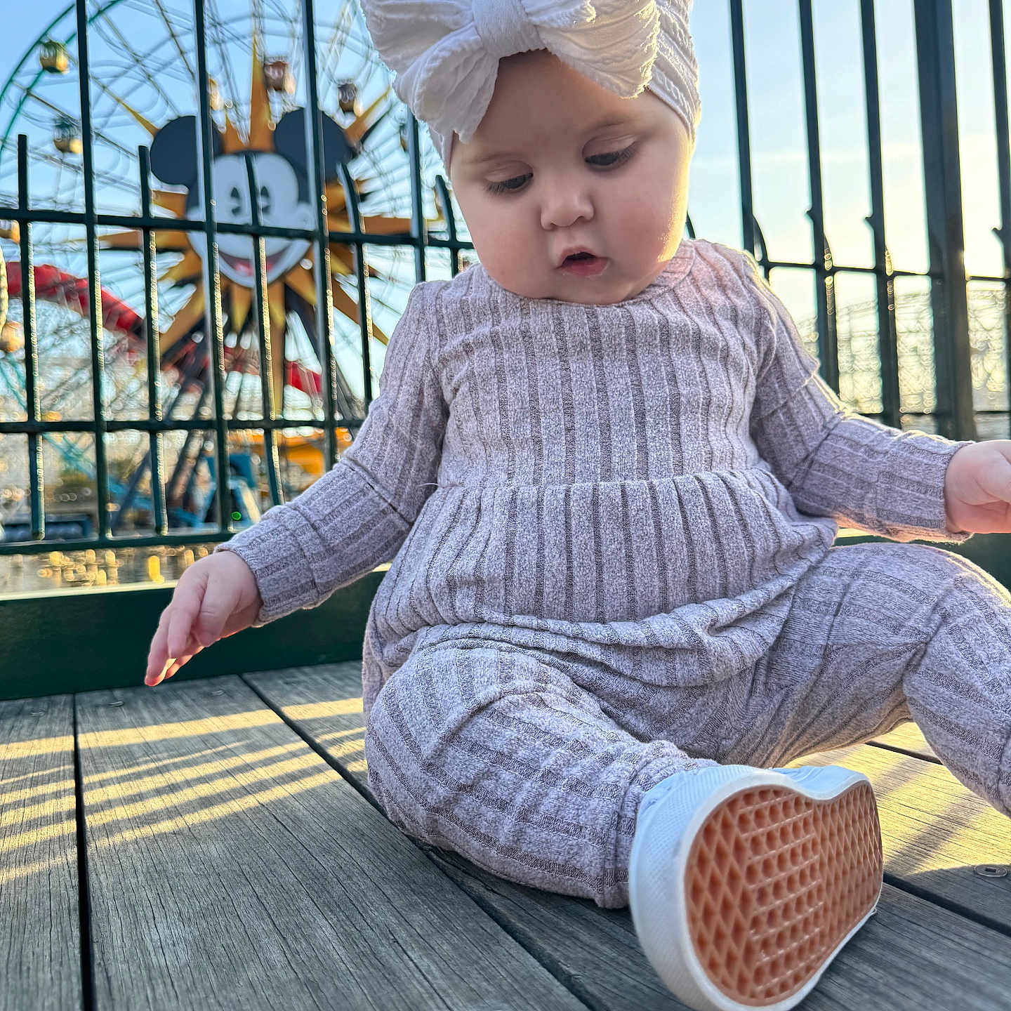 Oakley joined the competition — help win amazing prizes! amusement_park, baby, baby_fashion, bow, child, clothing, cute, daylight, ferris_wheel, headband, mickey_mouse, outdoor, person, playful, portrait, shoes, sitting, sunlight, toy, wooden_deck