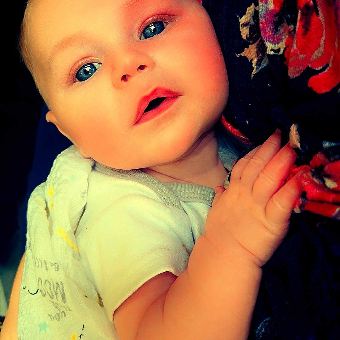 Garrett is registered to the contest to win money with this photo: baby, infant, child, face, blue_eyes, hand, blanket, clothing, floral_pattern, fabric, portrait, cute, skin, expression, closeup, soft_light, indoor, person, newborn, holding