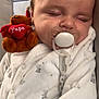 baby, sleeping, pacifier, plush_toy, teddy_bear, onesie, white_clothing, infant, cute, cozy, peaceful, child, face, soft_toy, resting, indoor, closeup, comfort, adorable, baby_sleeping