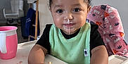 Ocean is registered to the contest to win money with this photo: toddler, child, highchair, cupcake, messy, food, frosting, crumbs, pink_cup, hair_buns, green_bib, black_shirt, indoor, table, face, hands, expression, happy, breaking_food, home