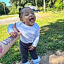 toddler, child, laughing, happy, outdoor, grass, sneakers, white_shirt, tattoo, hand_holding, basketball_hoop, pants, sunny_day, trees, playful, person, young_child, smiling, footwear, sidewalk