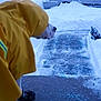 dog, yellow_raincoat, snow, winter, ice, car, driveway, outdoor, cold, steps, pet, animal, clothing, footwear, pavement, weather, side_view, canine, protective_gear, seasonal