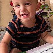 Cooper joined the competition — help win amazing prizes! toddler, child, smile, book, reading, indoors, pillow, buzz_lightyear, toy_story, striped_shirt, happy, face, hand, colorful, background, person, young_child, playful, seated, cute