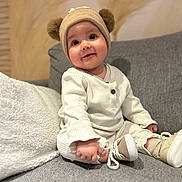 Marceau a rejoint le concours — aidez-le/la à gagner de superbes lots ! baby, child, hat, pom_poms, beige, cream, couch, gray, shoes, socks, smile, face, person, indoors, soft_texture, warm_lighting, clothing, seated, cute, portrait