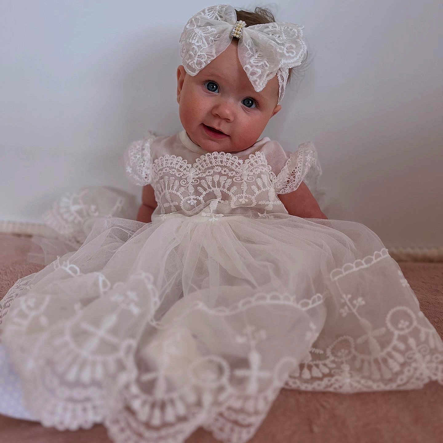 Clara is registered to the contest to win money with this photo: baby, blue_eyes, bow, child, clothing, cute, dress, face, fashion, headband, indoor, infant, lace, person, portrait, sitting, smile, soft_light, white, young