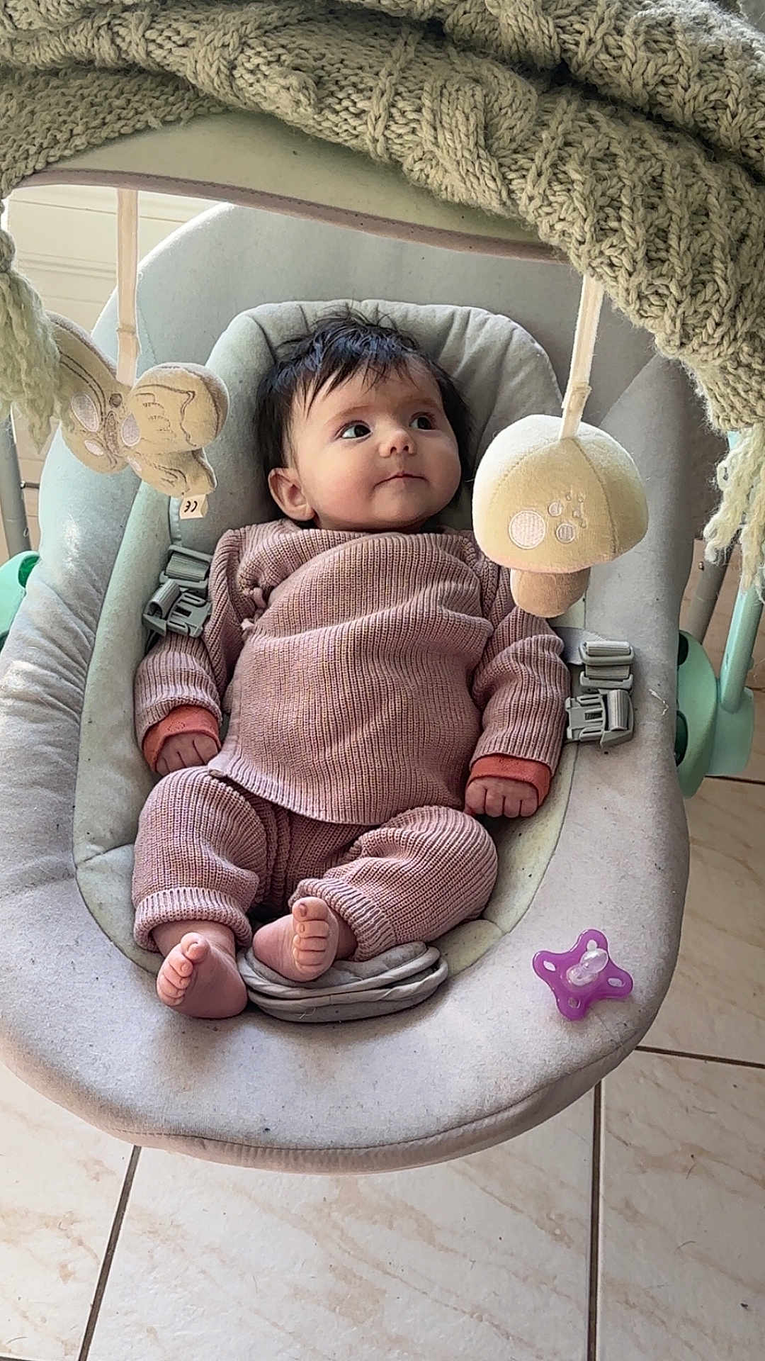 Rose participe au concours pour gagner de l'argent avec cette photo : baby, infant, baby_rocker, knit_clothing, plush_toy, pacifier, floor_tile, indoor, child, cute, soft_lighting, seat, baby_girl, baby_boy, hands, feet, looking_up, baby_accessory, comfort, home