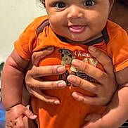 Ricardo joined the competition — help win amazing prizes! baby, infant, child, orange_onesie, smile, tongue_out, curly_hair, hands, holding, cute, portrait, person, skin, face, indoor, happy, chubby, close_up, expression, young