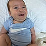 baby, smiling, infant, blue_onesie, white_pillow, quilted, cute, happy, child, person, sitting, indoors, soft_lighting, face, skin, mouth_open, expression, legs, arm, clothing