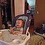 baby, high_chair, food, messy, smiling, indoor, child, face, clothing, tray, seat, floor, blanket, laundry_basket, door, room, household_items, wooden_floor, happy, infant