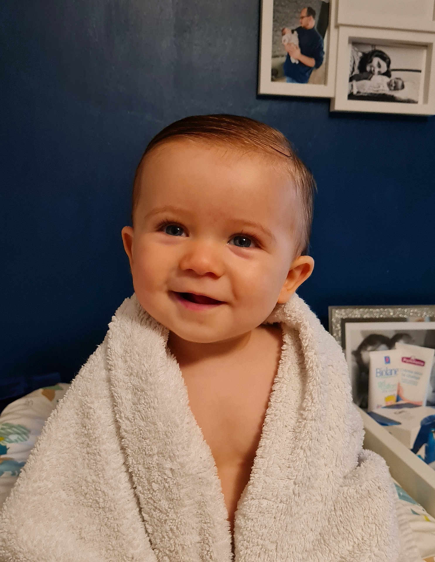 Nino participe au concours pour gagner de l'argent avec cette photo : baby, child, towel, smile, face, blue_wall, photograph, frame, indoor, person, skin, happy, portrait, young, cute, infant, wrapped, soft, background, home