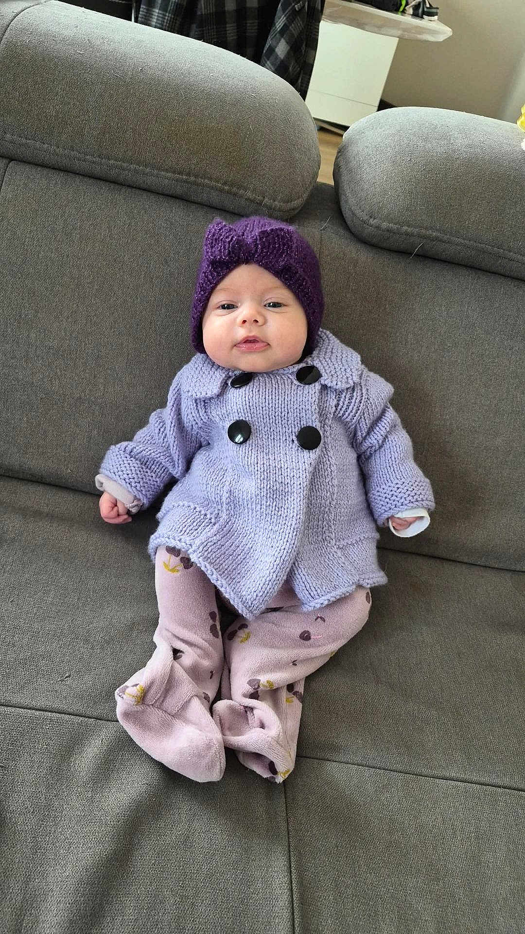 Lila a rejoint le concours — aidez-le/la à gagner de superbes lots ! baby, child, infant, purple_hat, knitted_coat, couch, sofa, home_interior, soft_toys, comfortable, pastel_colors, sitting, cute, face, portrait, warm_clothing, indoor, relaxed, furniture, legs