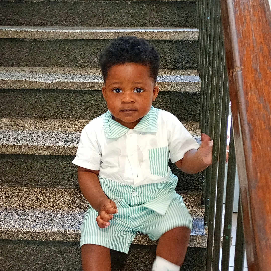 Ange Erane participe au concours pour gagner de l'argent avec cette photo : brown_hair, casual, child, concrete_stairs, curious, daylight, handrail, indoors, looking_at_camera, portrait, railing, shorts, single_child, sitting, socks, stairs, striped_clothing, toddler, white_shoes, young_child