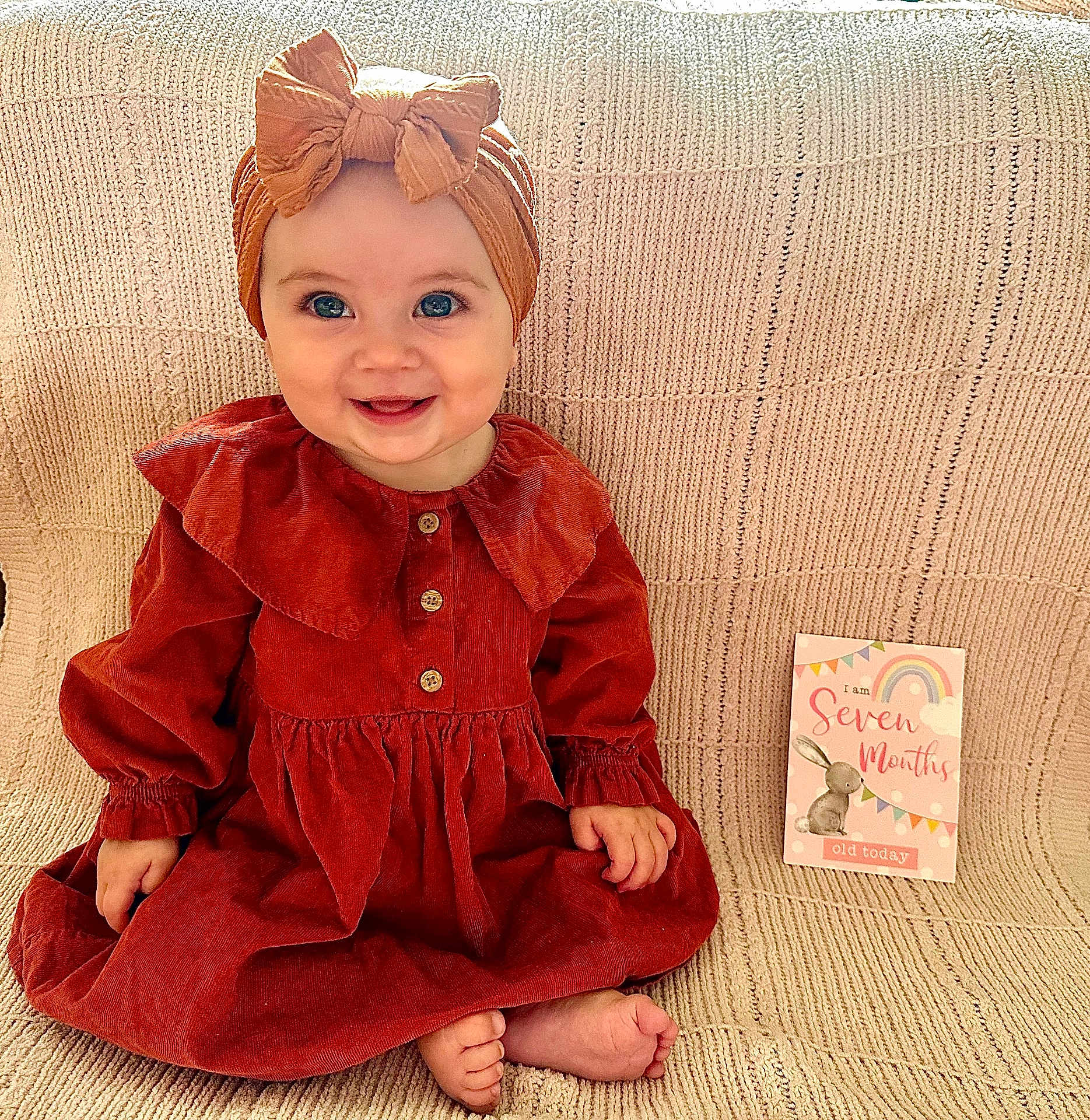 Cecelia joined the competition — help win amazing prizes! baby, child, girl, smile, headband, bow, dress, knitted_blanket, milestone_card, sitting, happy, cute, portrait, indoors, feet, hand, button, fabric, person, blue_eyes