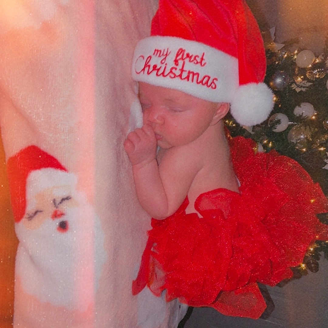 Zeanette is registered to the contest to win money with this photo: baby, blanket, christmas, christmas_tree, cute, decorations, festive, holiday, holiday_season, indoors, infant, lights, newborn, peaceful, red_tutu, santa_face, santa_hat, sleeping, soft_lighting, toddler