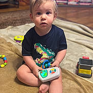 Parker joined the competition — help win amazing prizes! toddler, baby, child, sitting, blanket, toy, light_up_toy, truck, carpet, living_room, blond_hair, blue_eyes, shirt, graphic_tee, feet, playtime, portrait, looking_at_camera, indoor, curious_expression