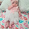 baby, infant, child, portrait, lying_down, pink_outfit, white_dress, headband, bow, smiling, face, eyes, blanket, alphabet_blanket, bed, indoors, textile, fashion, cute, photography