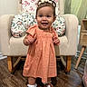 baby, chair, child, cushion, cute, dress, floral_pattern, furniture, hair_bows, happy, home, indoor, peach_color, portrait, shoes, smiling, socks, standing, toddler, wooden_floor