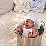 baby, infant, child, portrait, smiling, sitting, bucket, metal_container, teddy_bear, stuffed_animal, nursery, blanket, fluffy_rug, white_clothing, chef_hat, coin, cushions, indoor, milestone_photo, happy