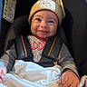 baby, infant, child, smiling, car_seat, car_interior, knitted_hat, winter_clothing, blanket, safety_harness, seated, portrait, face, hands, happy, indoors, vehicle, close_up, fabric, photography