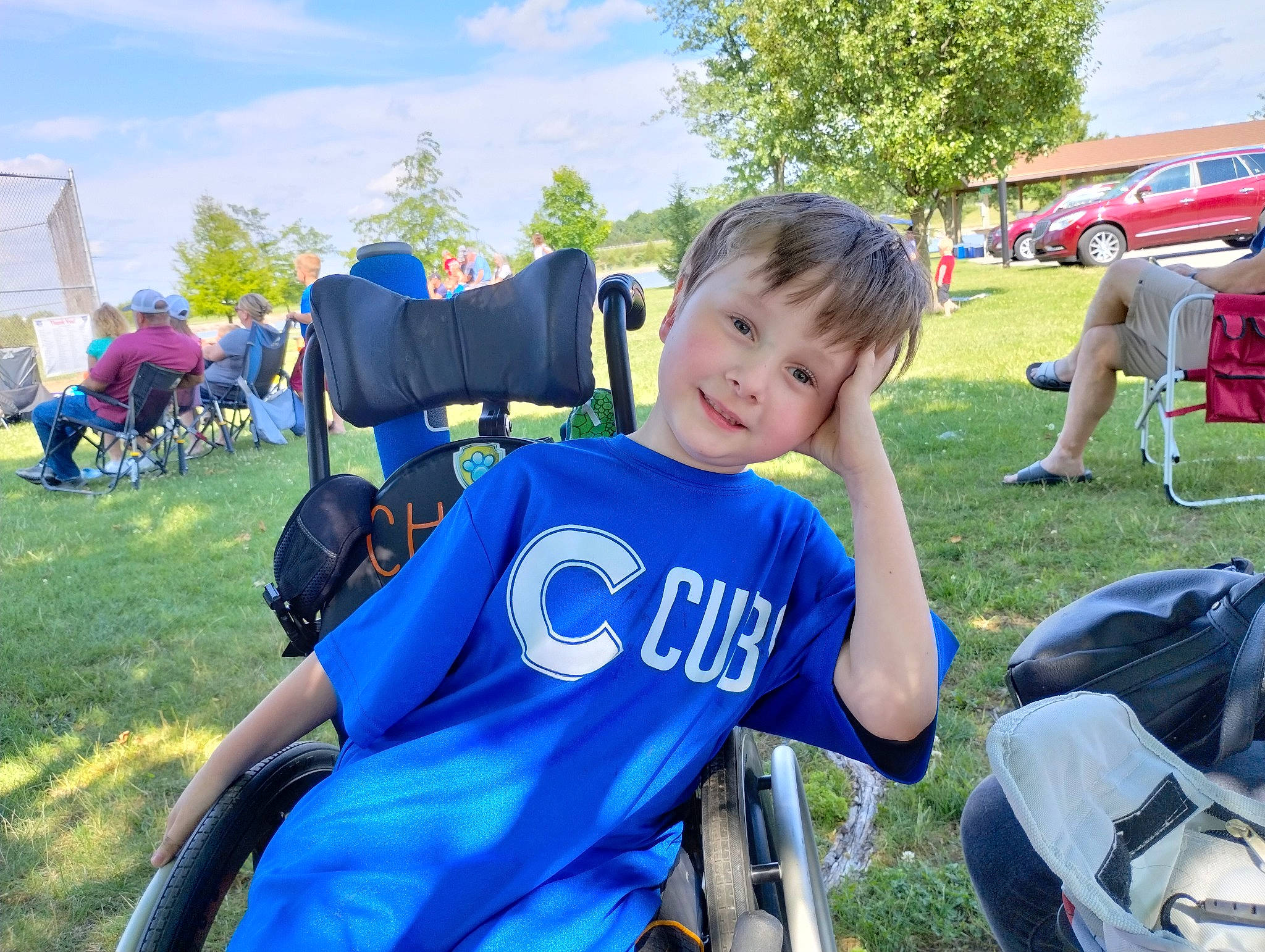 Charlie is registered to the contest to win money with this photo: backpack, bag, blue, chair, cloud, competition_event, electric_blue, event, grass, joy, leisure, luggage_and_bags, motor_vehicle, person, personal_protective_equipment, plant, recreation, shorts, sky, t_shirt