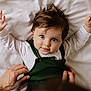baby, child, infant, hands, bed, white_bedspread, green_clothing, portrait, cute, looking_up, person, human, skin, face, eyes, hair, smiling, lying_down, tenderness, parent