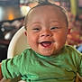 baby, child, smile, happy, green_shirt, blanket, high_chair, face, infant, indoors, cute, young, portrait, person, expression, seated, furniture, mohawk_hair, cheerful, closeup