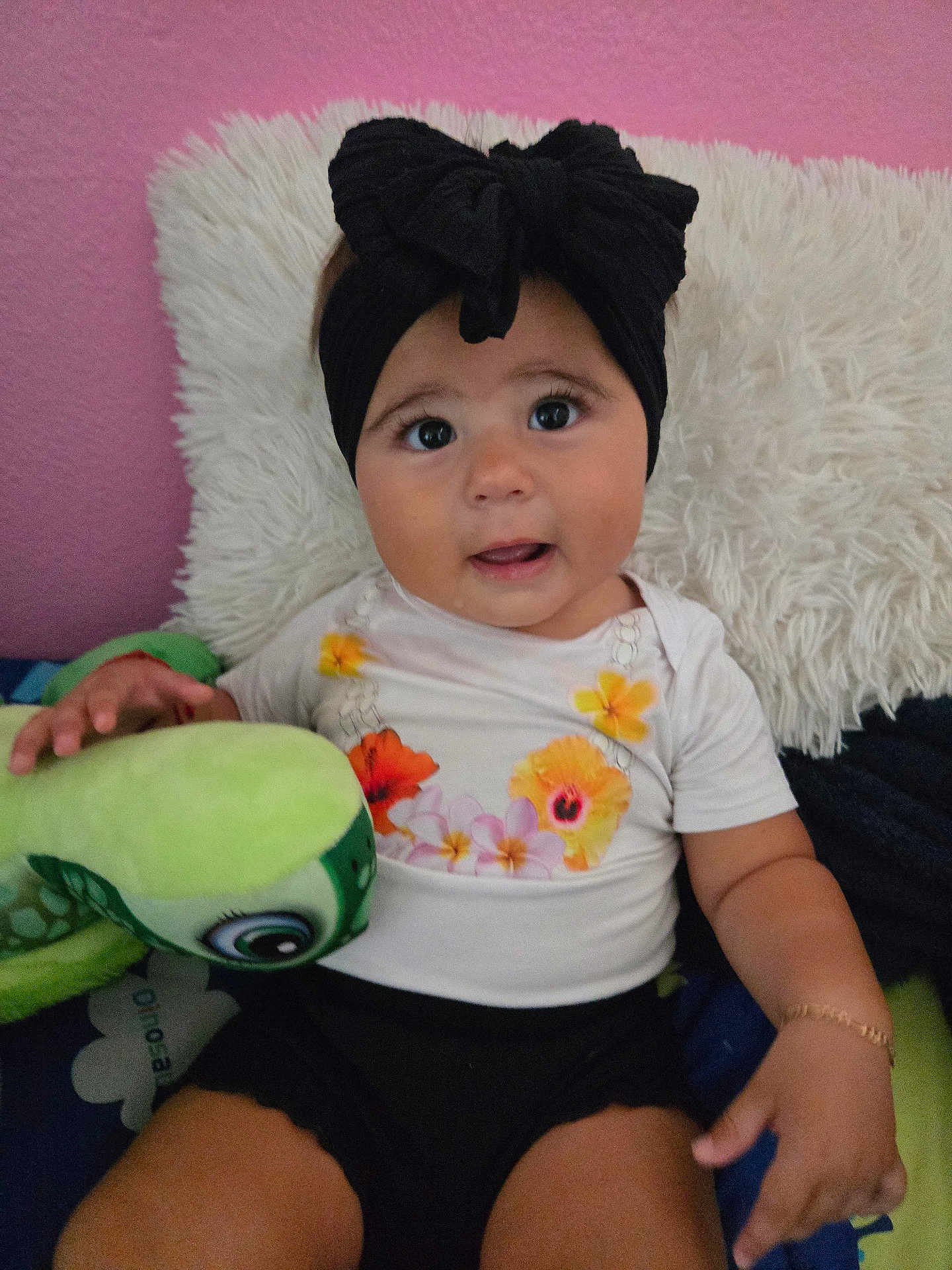 Eliana joined the competition — help win amazing prizes! baby, child, headband, bow, plush_toy, turtle, pillow, bed, pink_wall, black_shorts, white_shirt, floral_pattern, hand, cute, indoor, portrait, smiling, young_child, toy, curious