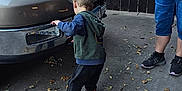 Hunter is registered to the contest to win money with this photo: child, toddler, vehicle, ford_truck, adult, sidewalk, autumn_leaves, outdoor, fence, casual_clothing, sneakers, hoodie, daylight, curious, person, concrete, tree, flag, parking, interaction