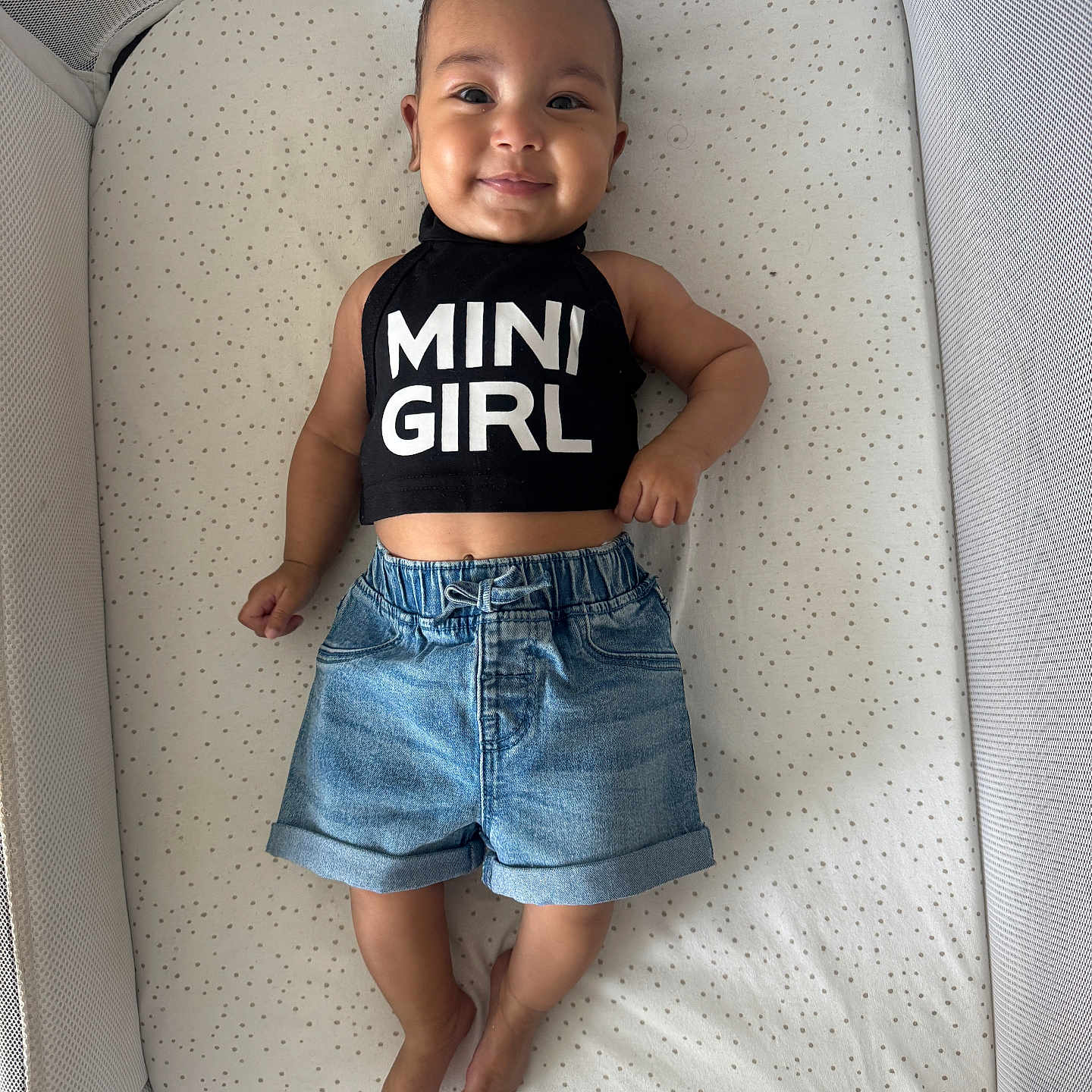 Elena Rose joined the competition — help win amazing prizes! baby, barefoot, black_top, casual_clothing, child, comfortable, crib, cute, denim_shorts, dots_pattern, fabric, happy, indoor, infant, person, portrait, sleeping_area, smile, text_clothing, young_child