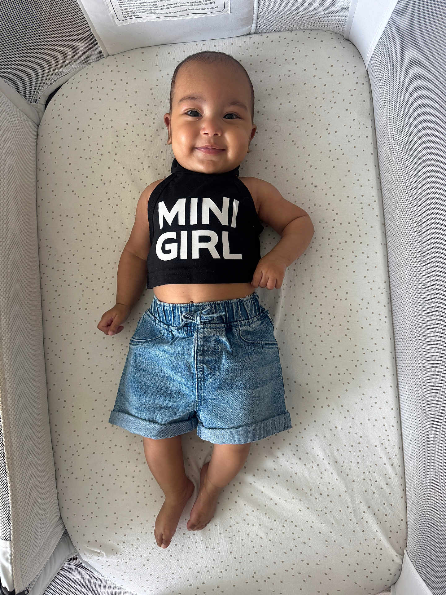 Elena Rose joined the competition — help win amazing prizes! baby, infant, smile, crib, denim_shorts, black_top, text_clothing, child, cute, happy, sleeping_area, fabric, dots_pattern, casual_clothing, barefoot, portrait, indoor, person, young_child, comfortable