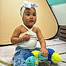bow, bracelet, casual_clothing, child, colorful, curly_hair, cute, expression, floor, headband, indoor, jeans, necklace, playful, plush_toy, portrait, sitting, toddler, white_top, young_child