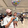 Elena Rose joined the competition — help win amazing prizes! man, baby, balloon, pink_cap, white_clothing, indoor, airport, people, crowd, tripod, photography, child, love, family, holding, curious, blue_outfit, smiling, waiting, public_space