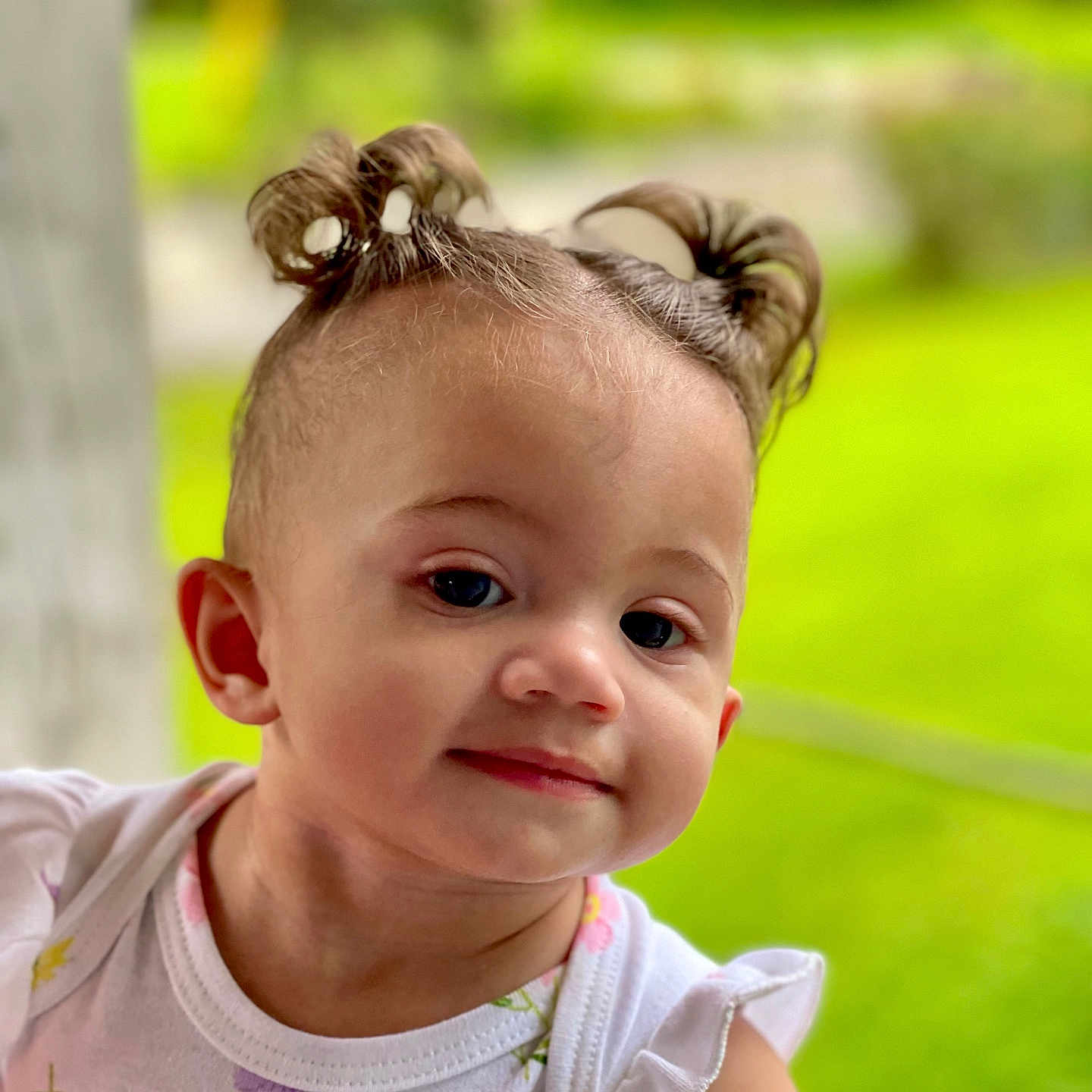 Belly is registered to the contest to win money with this photo: baby, child, closeup, curious, cute, daylight, face, floral_pattern, green_background, hair_buns, head, outdoor, person, portrait, skin, smiling, summer, toddler, white_clothing, young_child