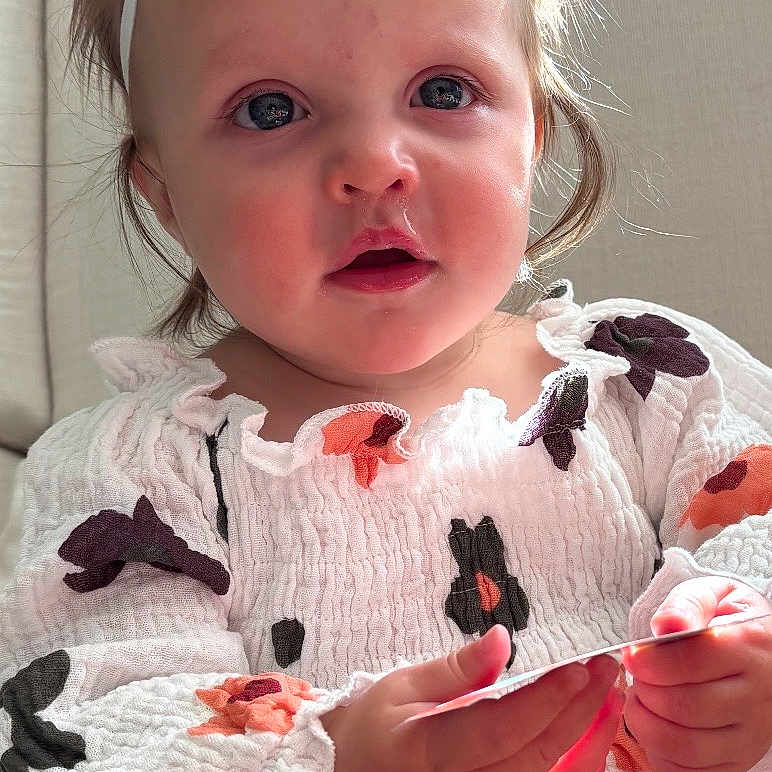 Leva joined the competition — help win amazing prizes! baby, child, clothing, couch, curious, cute, dress, expression, floral, hands, headband, indoor, light, natural_light, person, portrait, sitting, smiling, toddler, young_child