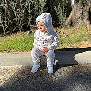 Lino a rejoint le concours — aidez-le/la à gagner de superbes lots ! toddler, child, hoodie, white_clothing, sitting, outdoor, sidewalk, curb, trees, greenery, sunlight, shadow, casual, footwear, contemplative, nature, park, young_child, casual_wear, daylight