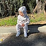 toddler, child, hoodie, white_clothing, sitting, outdoor, sidewalk, curb, trees, greenery, sunlight, shadow, casual, footwear, contemplative, nature, park, young_child, casual_wear, daylight