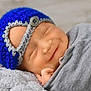 newborn, baby, sleeping, smiling, knitted_hat, blue_hat, gray_blanket, wrapped, cozy, soft_texture, infant, peaceful, cute, portrait, closeup, hand, resting, indoors, warm, child