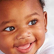 Kenza is registered to the contest to win money with this photo: baby, smiling, infant, face, closeup, white_clothing, happy, cute, child, portrait, skin, eyes, mouth, tongue, curly_hair, cheeks, expression, person, indoors, young
