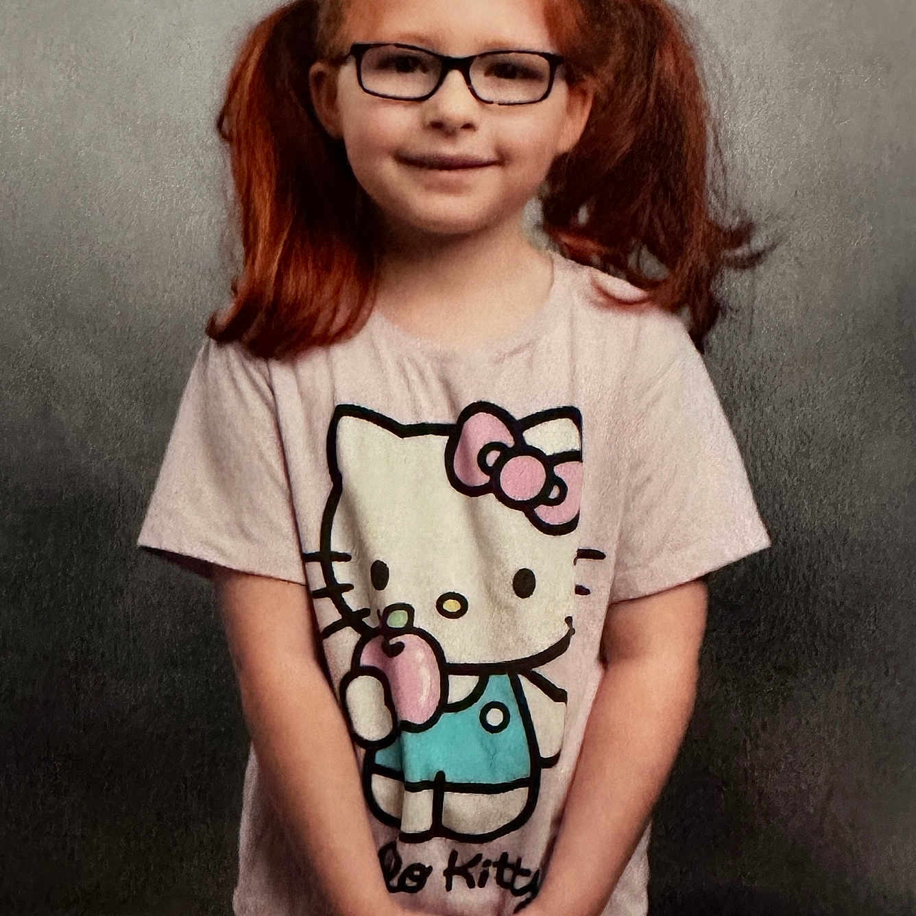 Chloe joined the competition — help win amazing prizes! child, girl, pigtails, red_hair, glasses, hello_kitty, tshirt, smile, standing, portrait, casual_clothing, cute, young, happy, studio_background, hands_clasped, innocent, fashion, person, kid